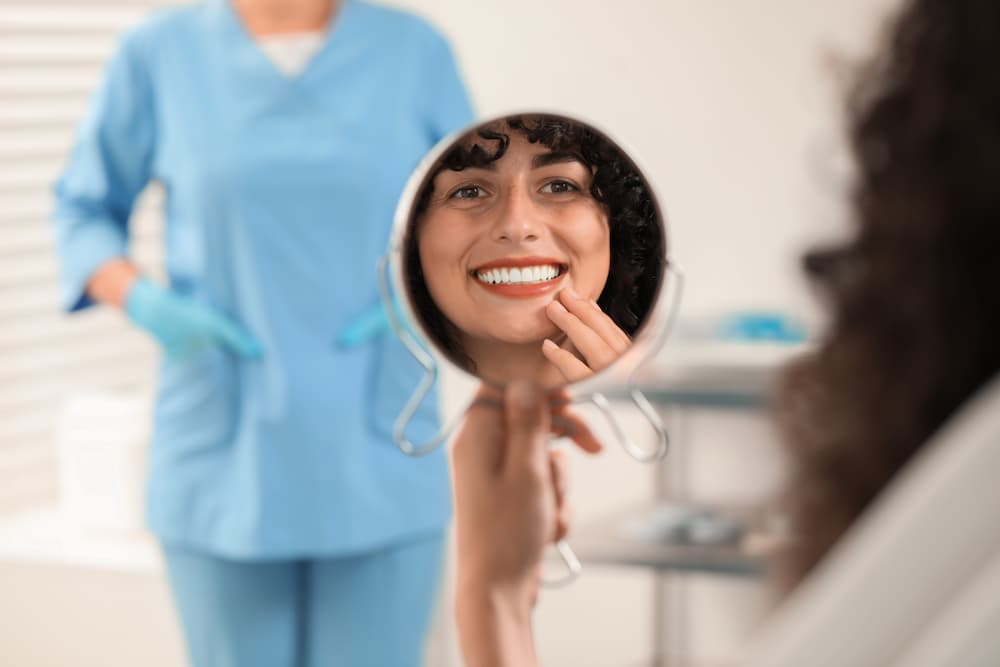 Woman reviewing her smile makeover in a mirror, promoting Texas cosmetic dentistry services like veneers or whitening.